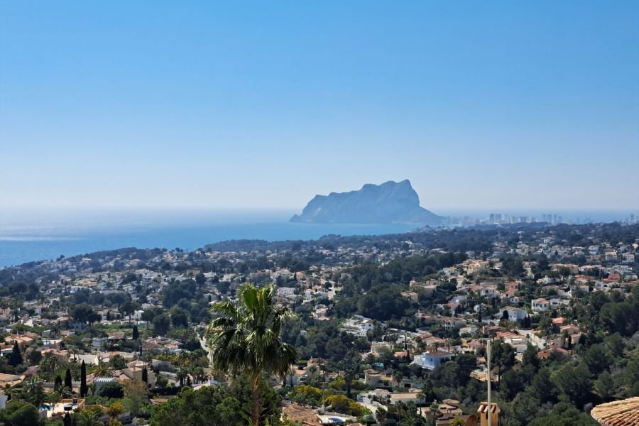 Panoramic elevated view of Benissa Costa residential area with luxury villas, Mediterranean vegetation, and the iconic Peñón de Ifach rock on the skyline under a clear blue sky