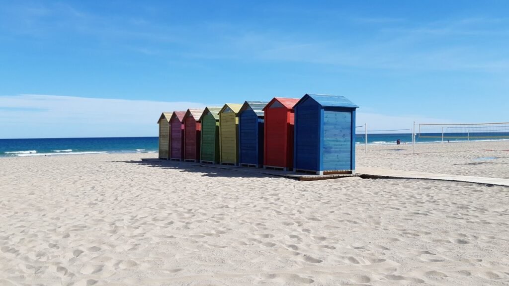 Row of vibrant colorful wooden beach huts on the sandy shore of Playa de San Juan in Alicante under a clear blue sky